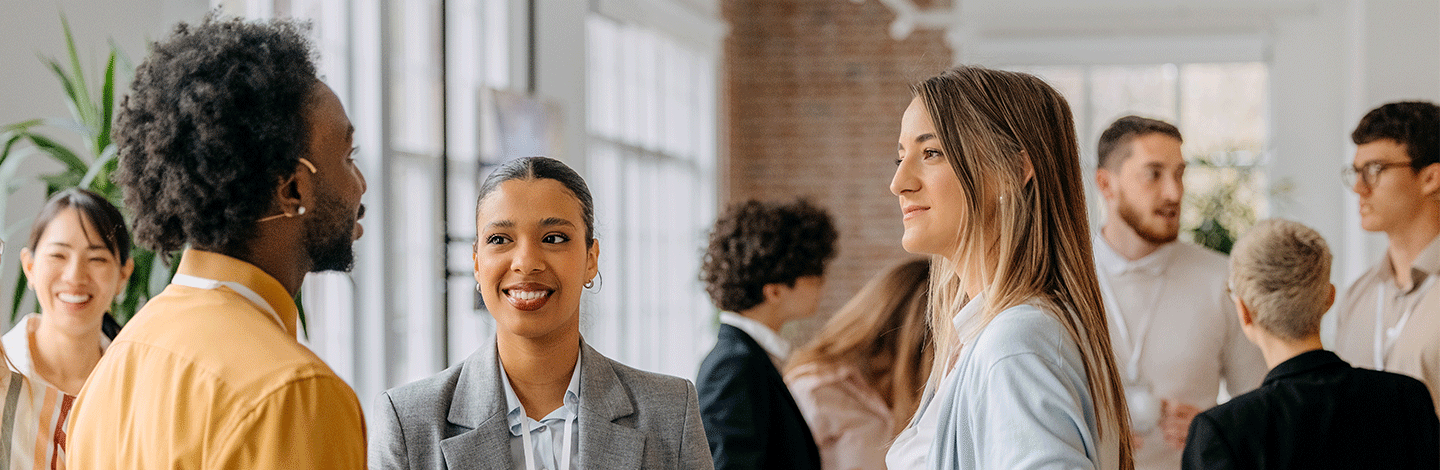 Diverse group of professionals engaged in conversation in a bright, modern office space with exposed brick walls.