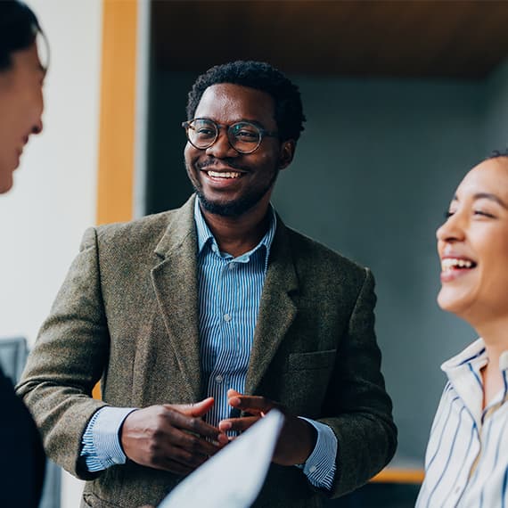 Smiling professional man in glasses and blazer engaged in conversation with colleagues in modern office setting