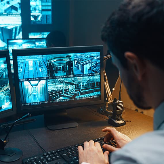 Person monitoring multiple security camera feeds on computer screens showing various building corridors and hallways.
