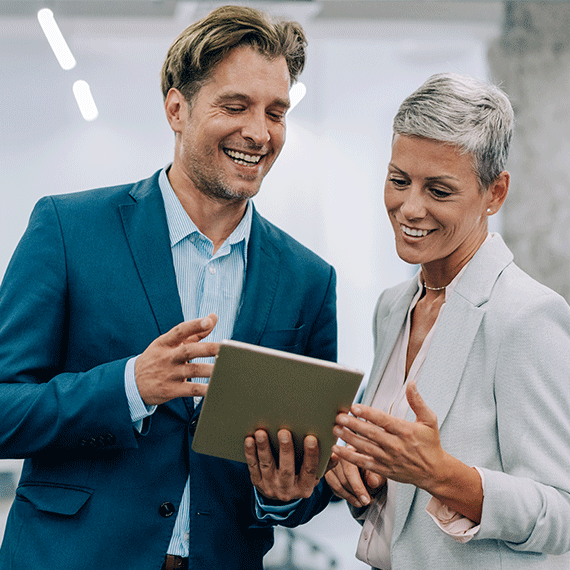 Two smiling business professionals in suits looking at a tablet together in an office setting